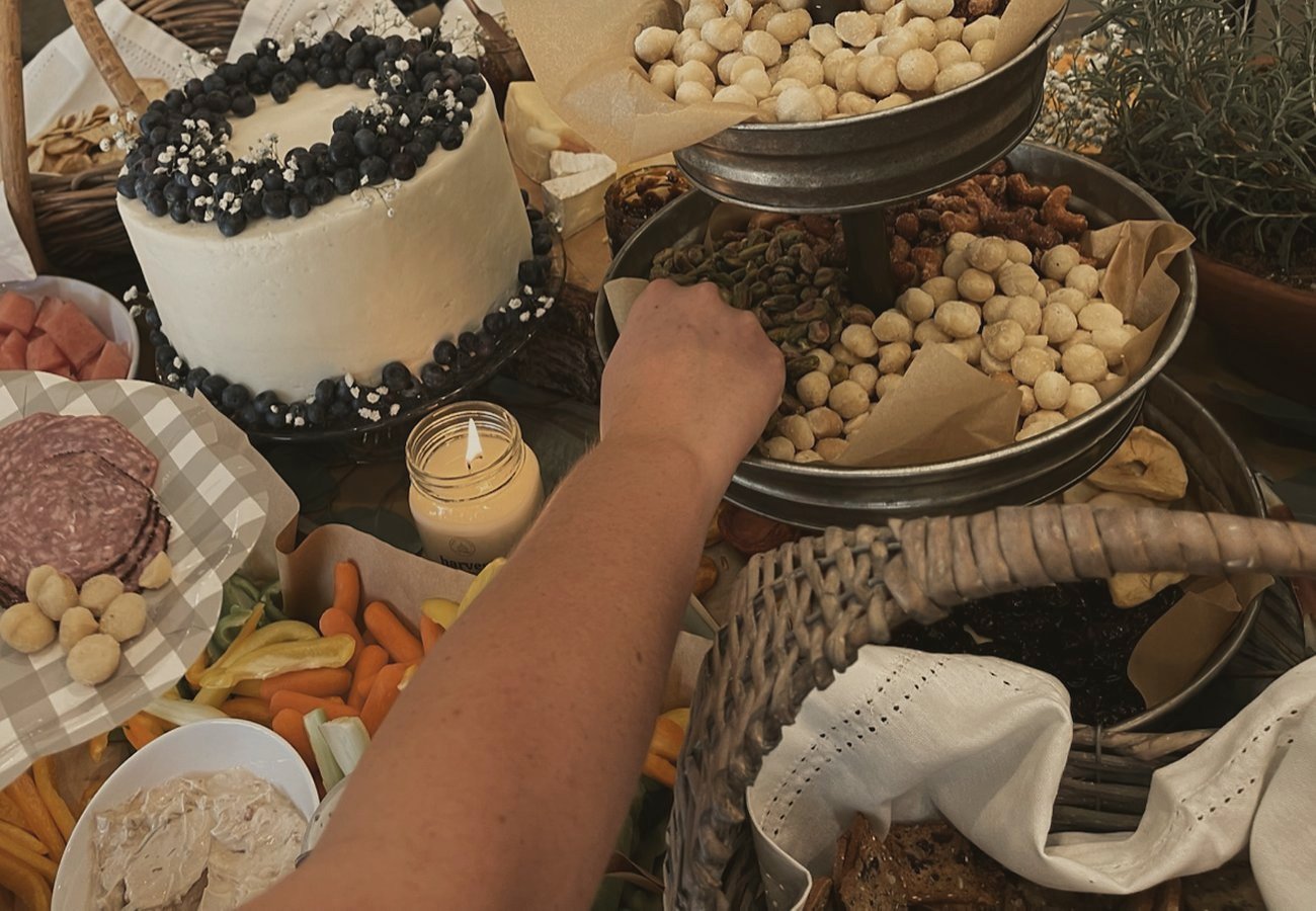 A frosted cake crowned with blueberries beside baskets of snacks