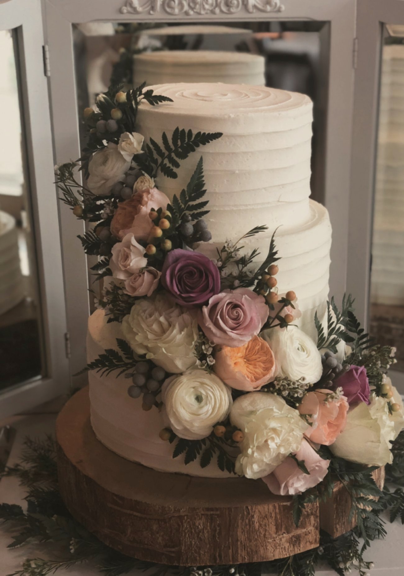 A two-tier textured buttercream cake with garden roses, ferns and berries