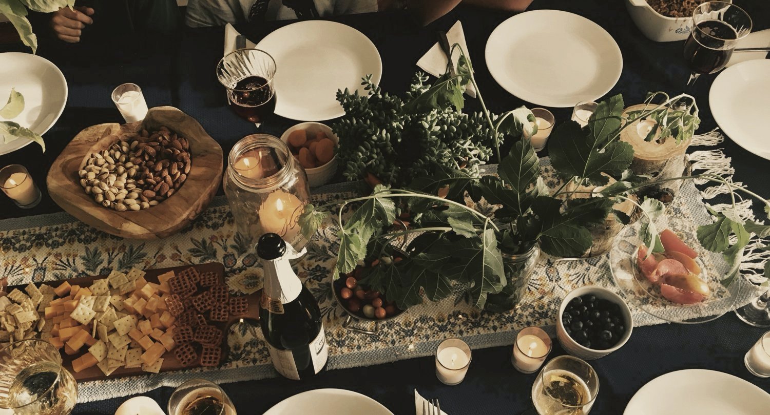 A candlelit table from above, with an olive wood bowl, a charcuterie board and votives
