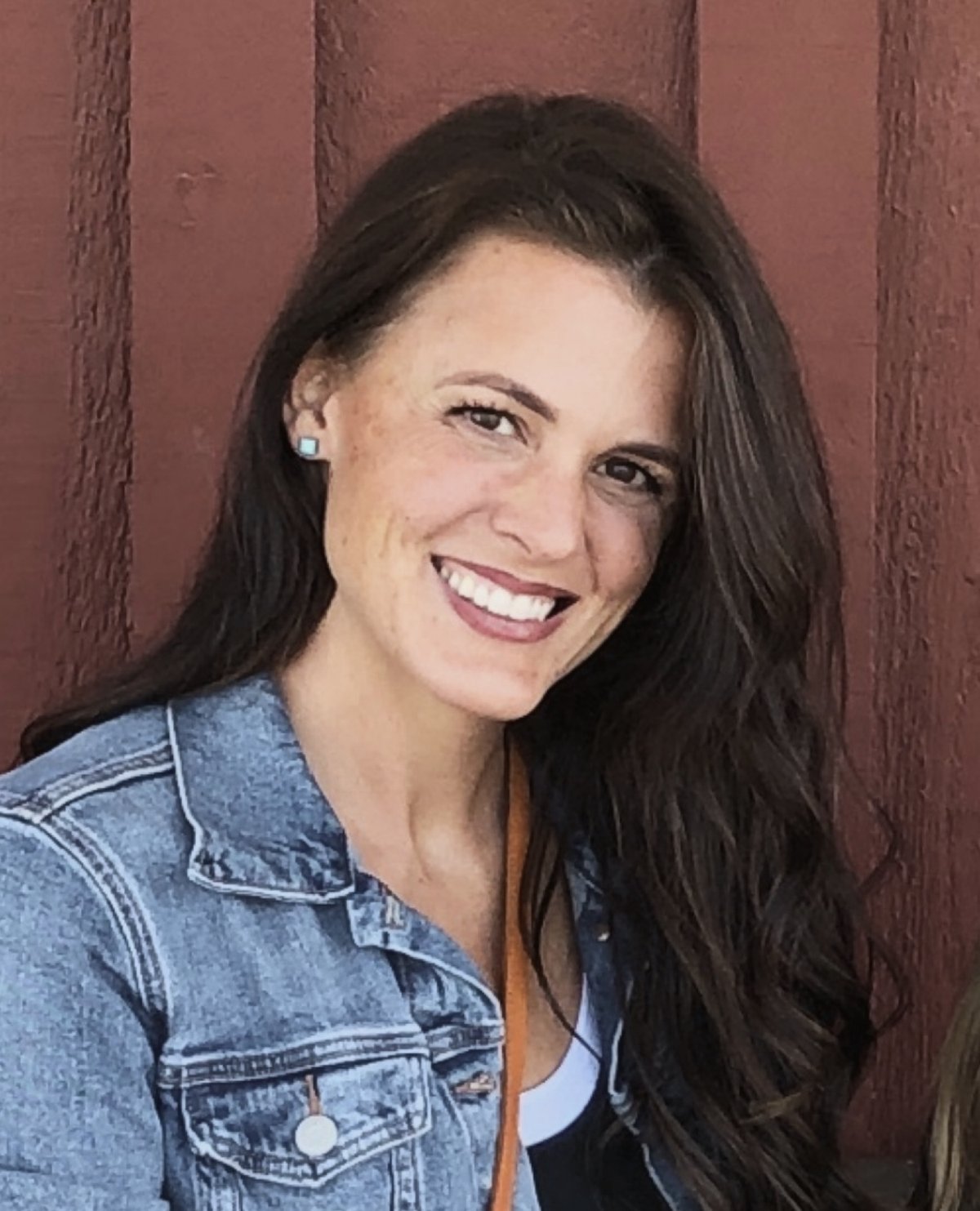 Rachel smiling in a denim jacket against a red barn wall