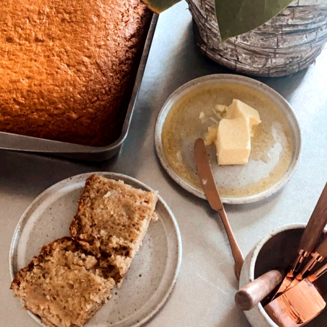 A pan of Grandma’s banana cake with buttered slices on a stoneware plate