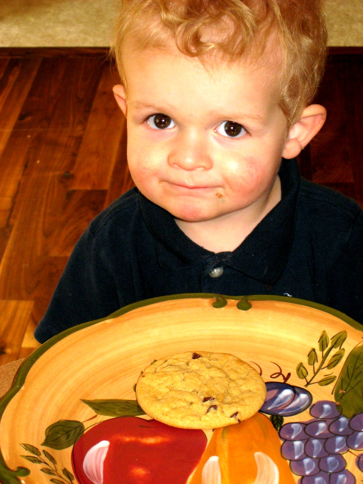 A little boy with a chocolate chip cookie on a painted fruit plate